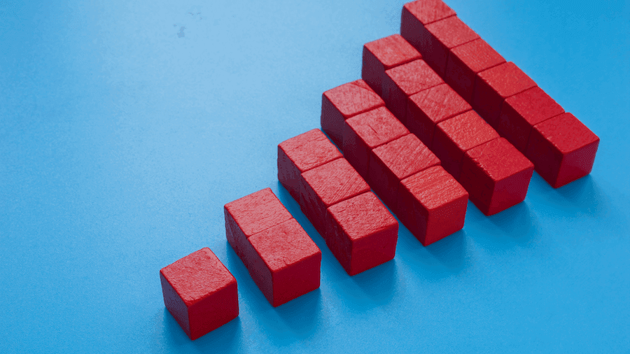 Red blocks arranged in a staircase pattern on a blue background, symbolizing growth or progression. The blocks increase in size from left to right.