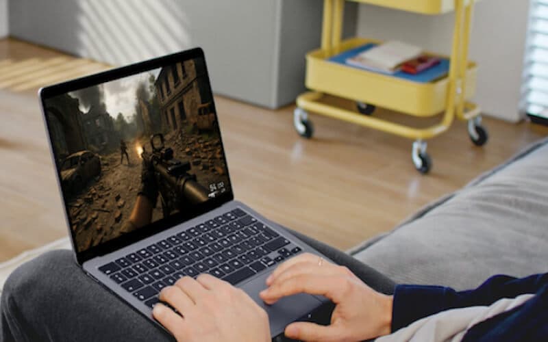 A person seated on a couch using a laptop, symbolizing game server hosting for multiplayer titles with customizable settings.