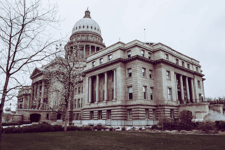 Grand stone building with a large domed roof and tall columns, surrounded by leafless trees and green lawn, under an overcast sky. Majestic and historical.