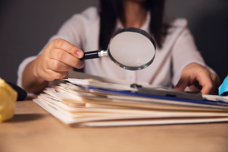 A person examining documents with a magnifying glass, representing detailed investigation or auditing.