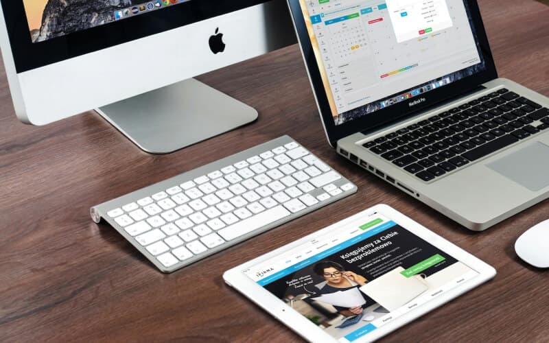 A laptop, tablet, and keyboard on a wooden desk, representing web hosting and application deployment services for digital agencies.